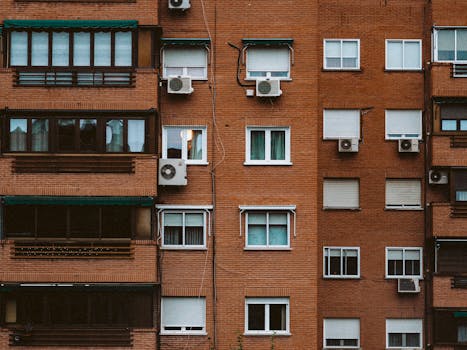 A detailed view of an orange brick apartment facade with windows and air conditioners.